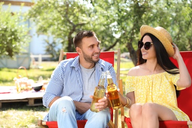 Smiling friends clinking bottles on picnic in park on summer day