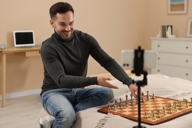 Photo of Teacher near chessboard conducting online lesson at home. Time for hobby