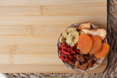 Photo of Wicker basket with different dried fruits on wooden board, top view. Space for text