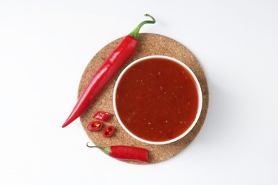 Photo of Spicy chili sauce in bowl and fresh peppers on white background, top view