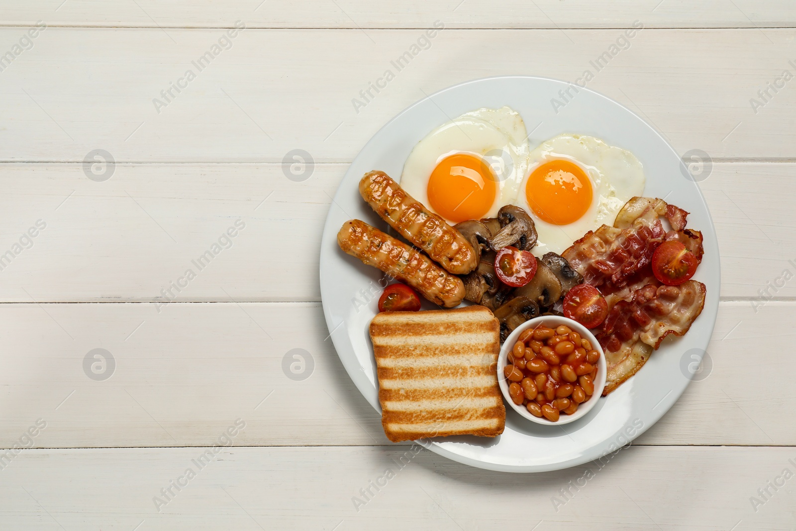 Photo of Plate of fried eggs, sausages, mushrooms, beans, bacon and toast on white wooden table, top view with space for text. Traditional English breakfast