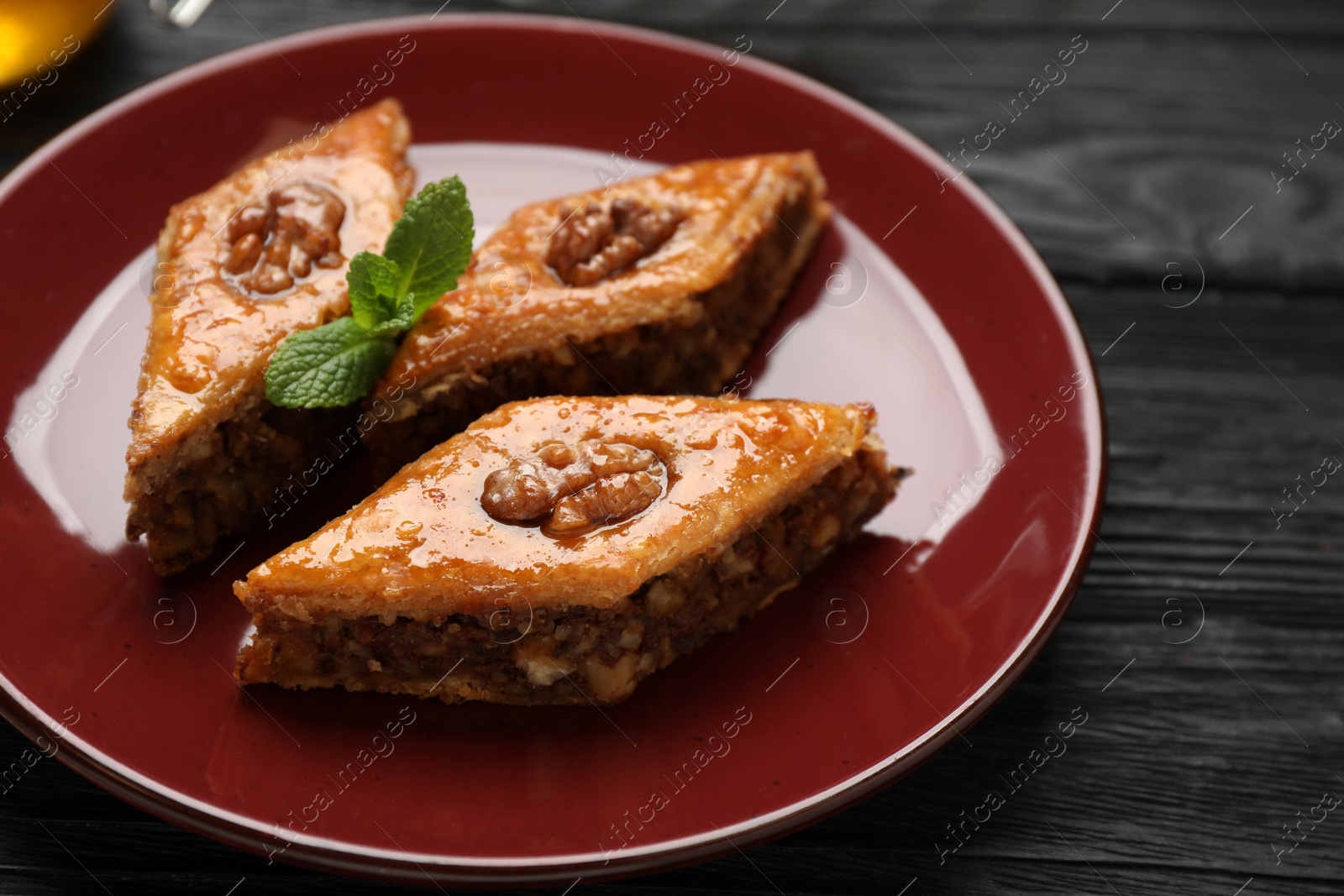 Photo of Delicious sweet baklava with walnuts and mint on black wooden table, closeup