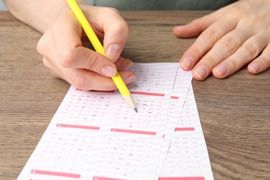 Photo of Woman filling out lottery tickets with pencil on wooden table, closeup