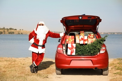 Photo of Authentic Santa Claus near car with open trunk fullpresents and fir tree outdoors