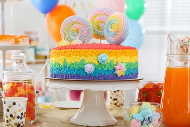 Photo of Bright birthday cake and other treats on table in decorated room