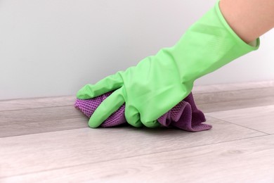 Photo of Woman in protective glove cleaning plinth with washcloth indoors, closeup