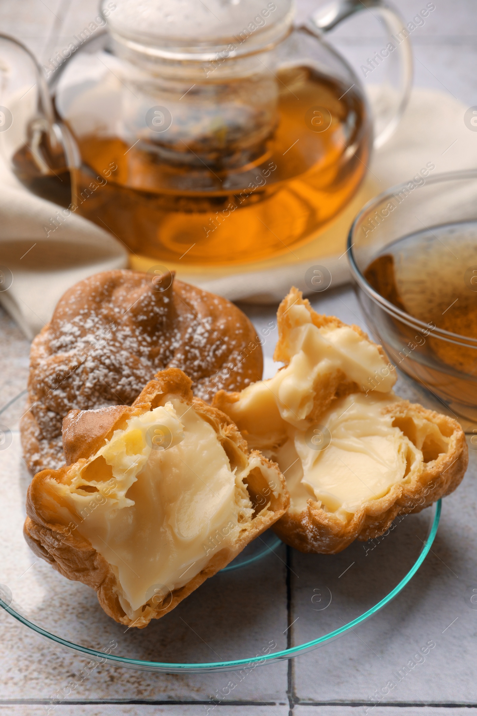 Photo of Delicious profiteroles filled with cream and tea on white tiled table, closeup