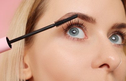 Photo of Beautiful woman applying mascara on pink background, closeup