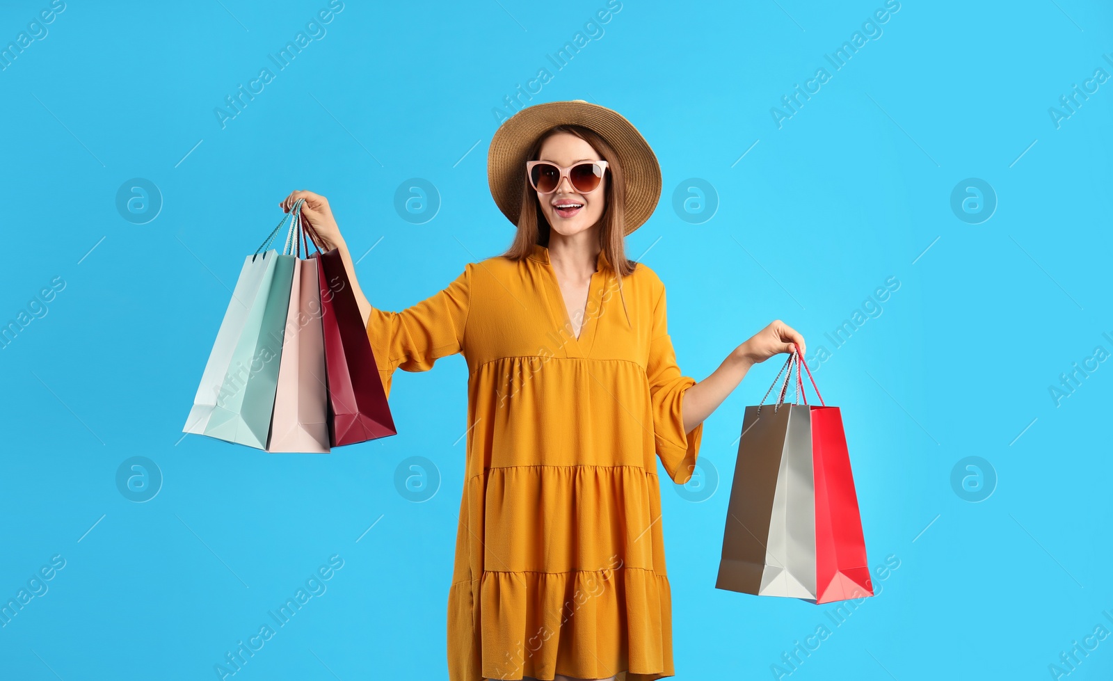 Photo of Beautiful young woman with paper shopping bags on light blue background