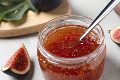 Jar with tasty fig jam and fresh fruits on white table, closeup