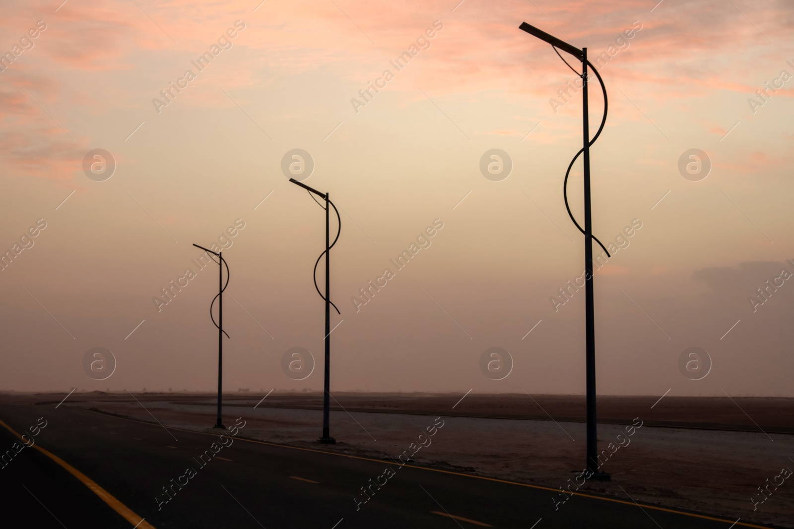 Photo of Street lights near empty road in desert at sunset