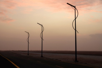 Street lights near empty road in desert at sunset