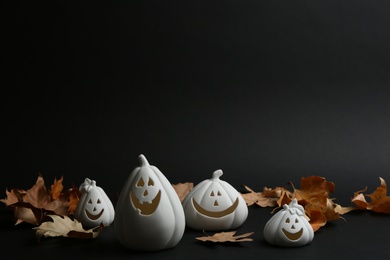 Photo of Jack-o-Lantern candle holders and fallen leaves on black background. Halloween decor