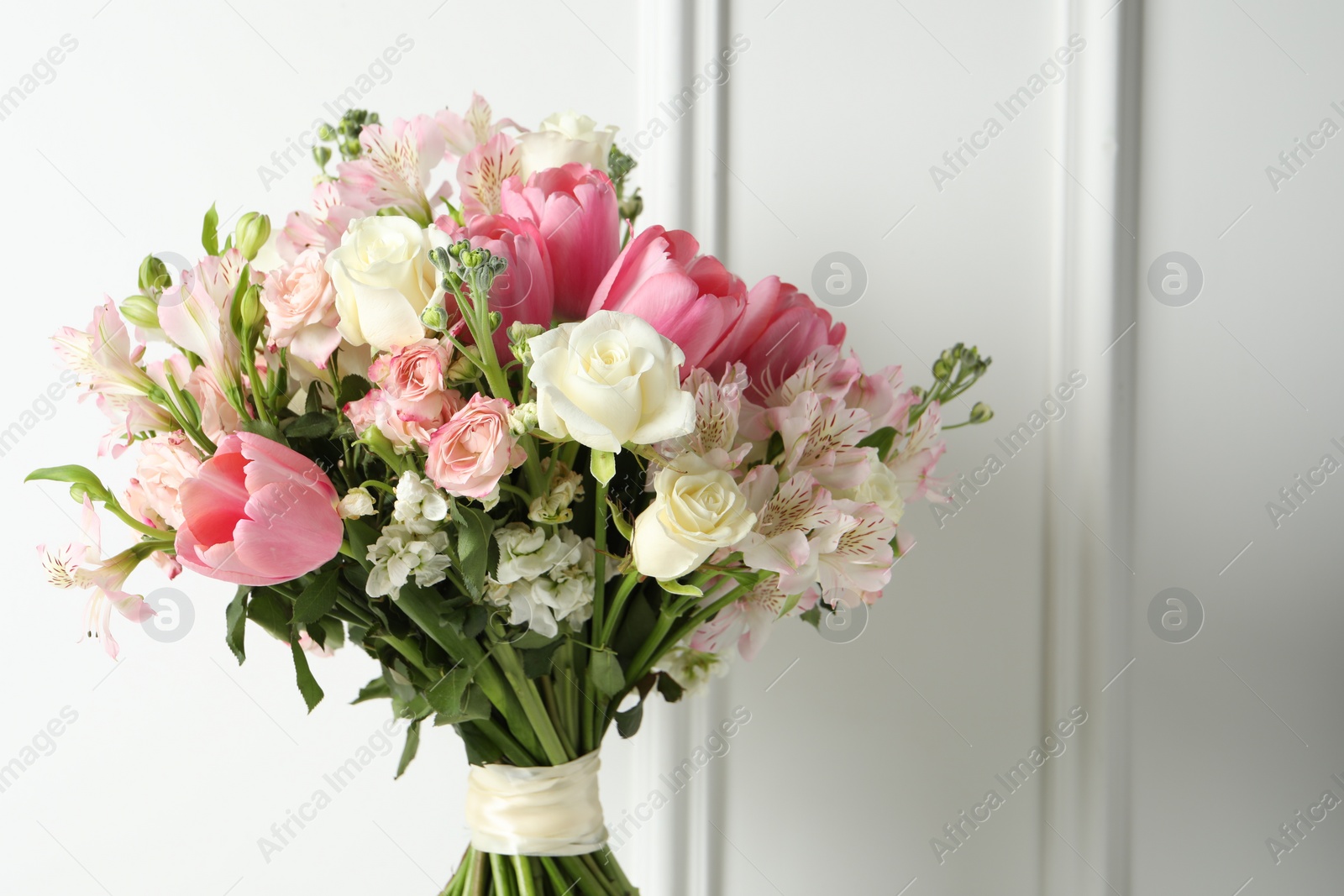 Photo of Beautiful bouquet of fresh flowers near white wall. Space for text