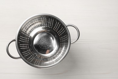 Metal colander on white wooden table, top view. Space for text