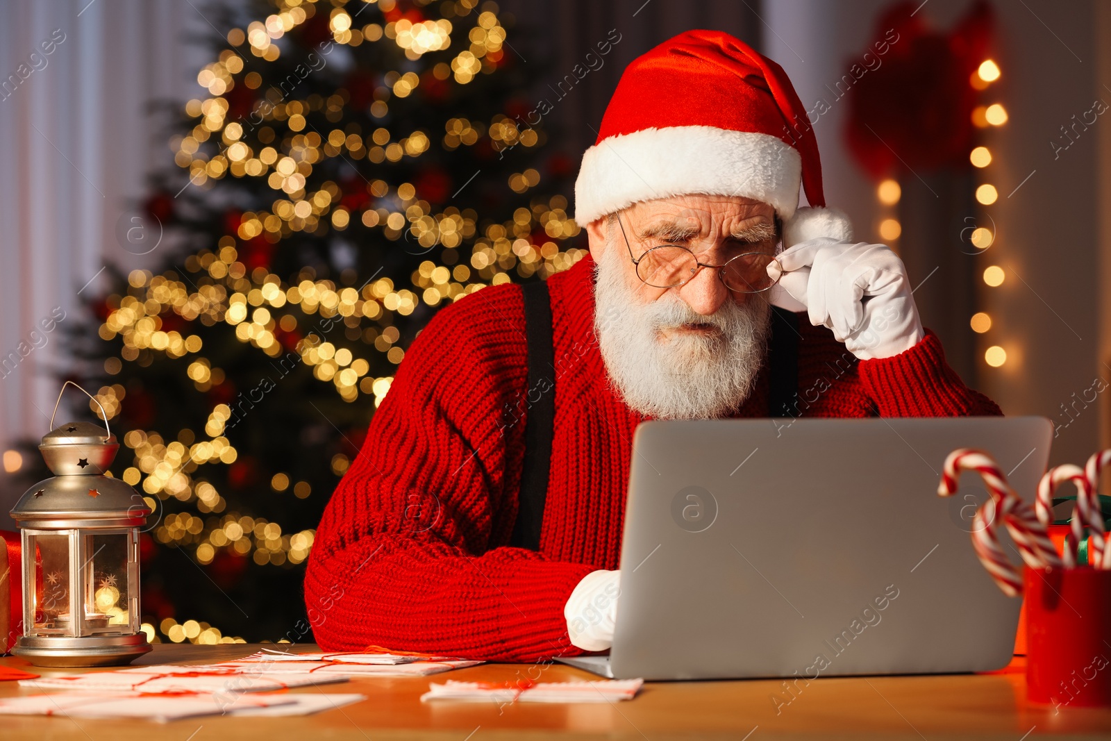 Photo of Santa Claus using laptop at his workplace in room with Christmas tree