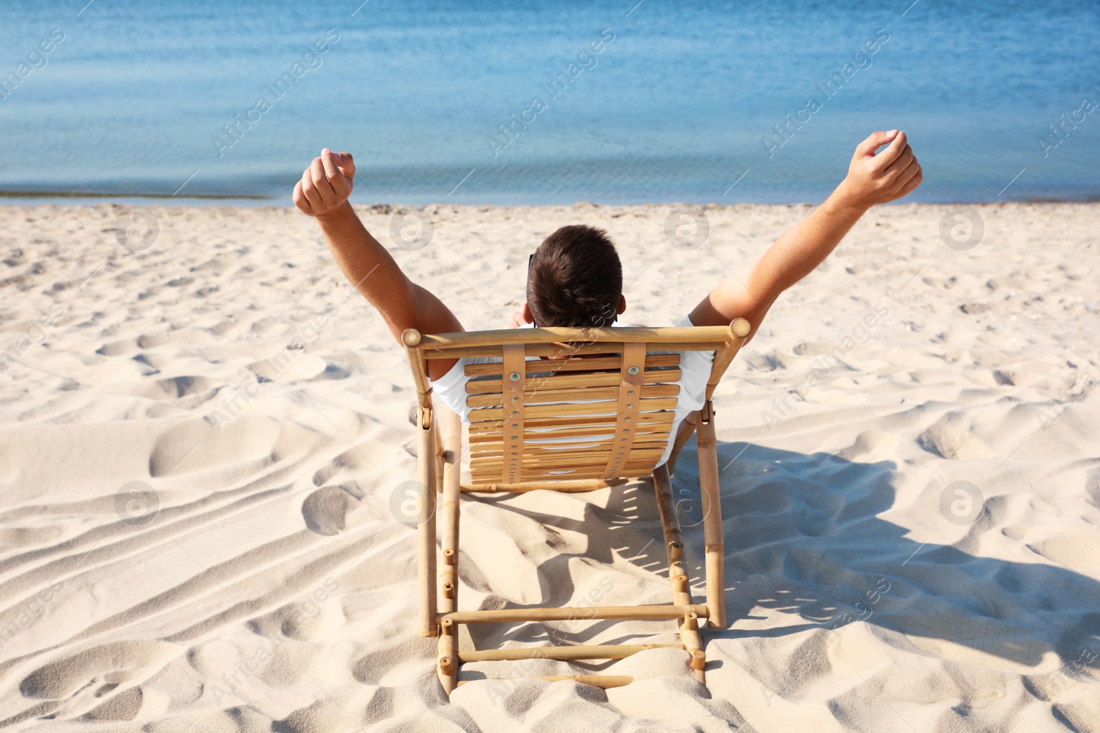 Photo of Young man relaxing in deck chair on sandy beach