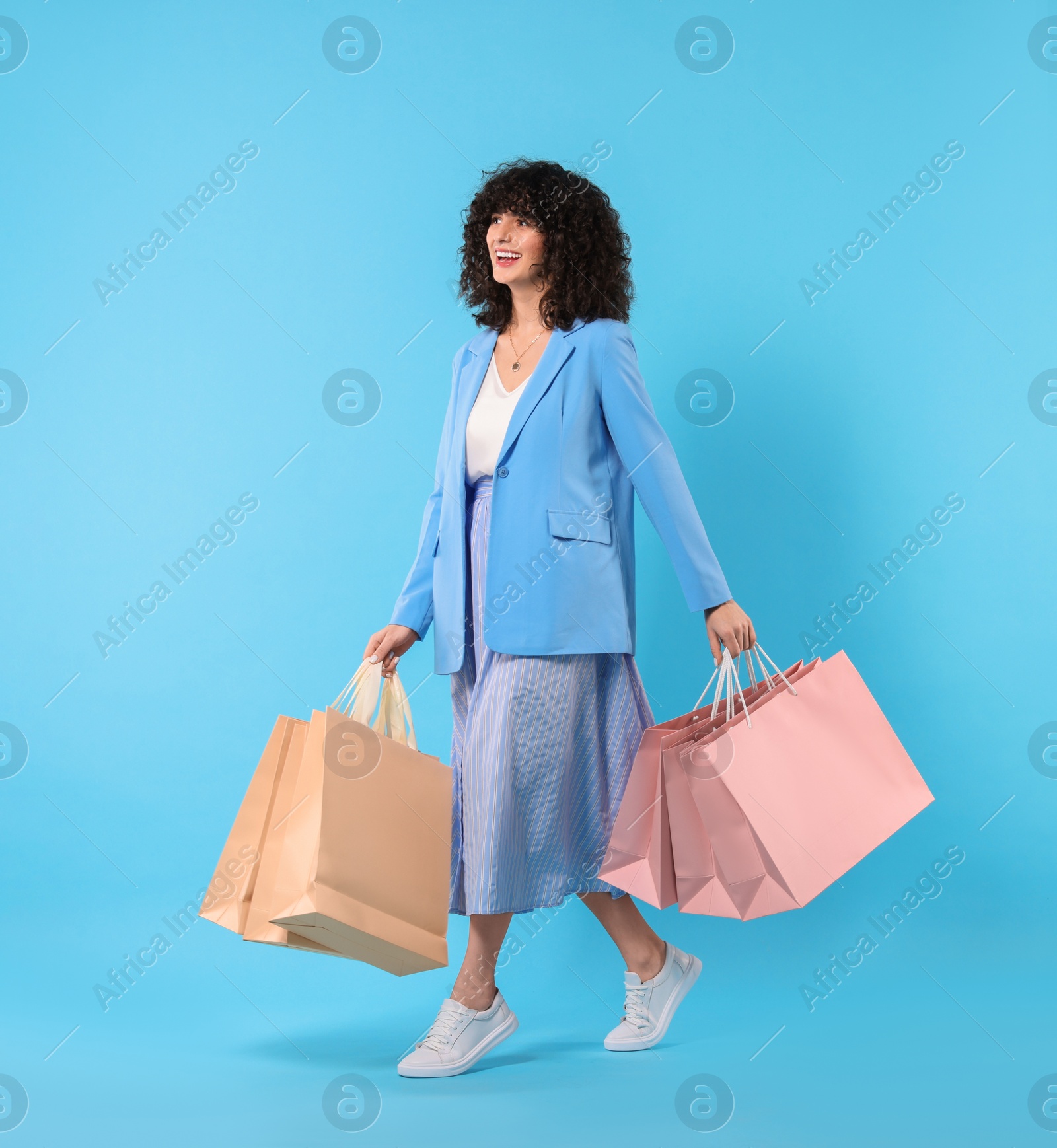 Photo of Happy young woman with shopping bags on light blue background