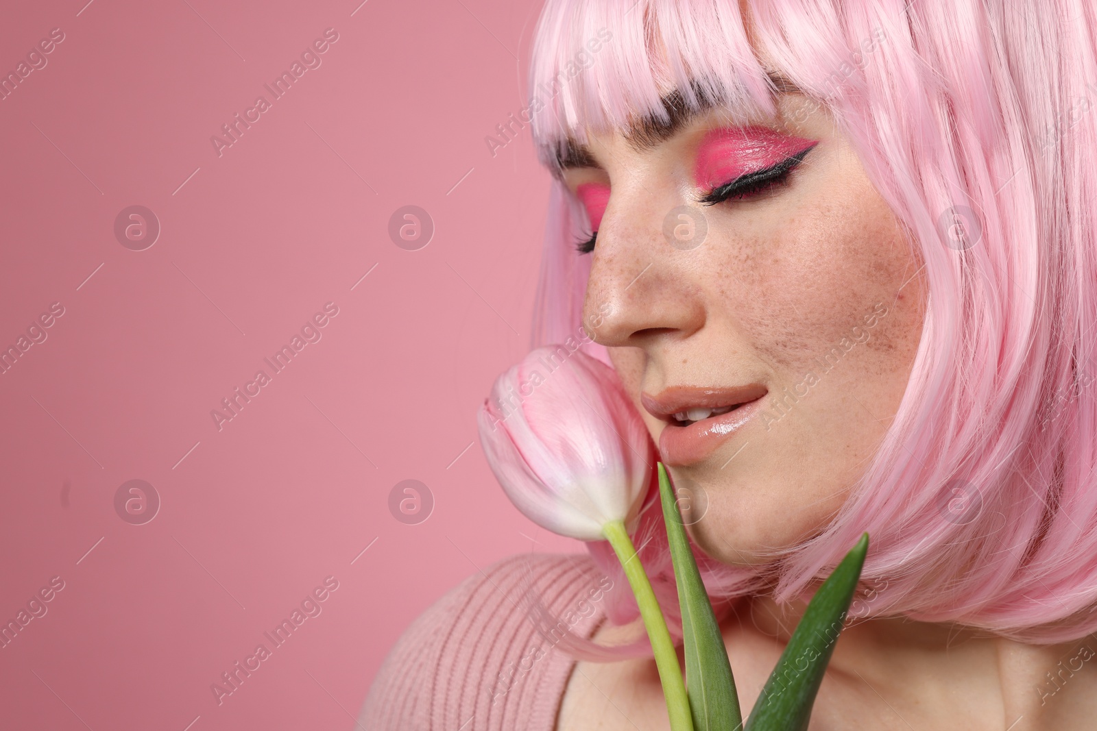 Photo of Beautiful woman with bright makeup, fake freckles and tulip on pink background, closeup. Space for text