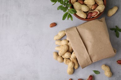 Paper bag with fresh unpeeled peanuts and leaves on grey table, flat lay. Space for text