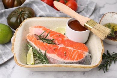 Fresh fish, lime, rosemary and marinade in baking dish on light marble table, closeup