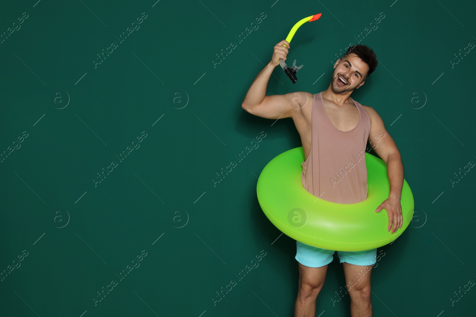 Photo of Funny young man with bright inflatable ring on dark green background, space for text