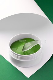Photo of Jar of under eye patches with spoon on color background. Cosmetic product