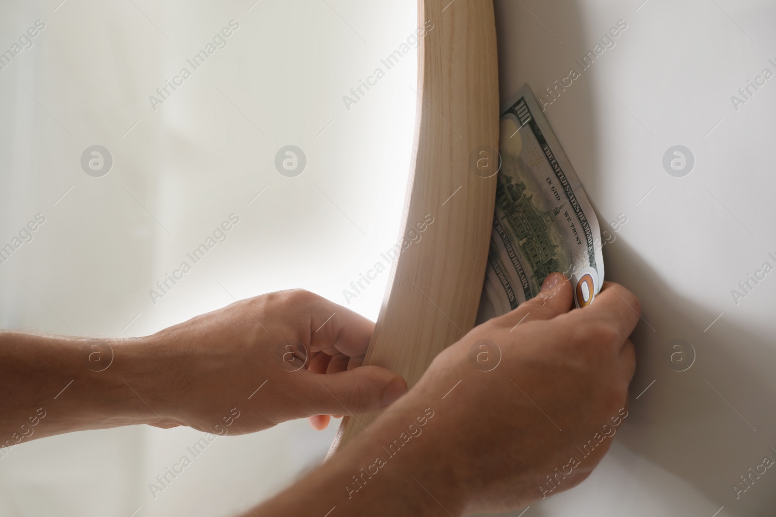 Photo of Man hiding money behind mirror indoors, closeup. Financial savings