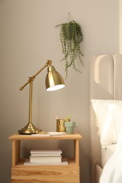 Photo of Stylish golden lamp and stationery on wooden nightstand in bedroom. Interior element