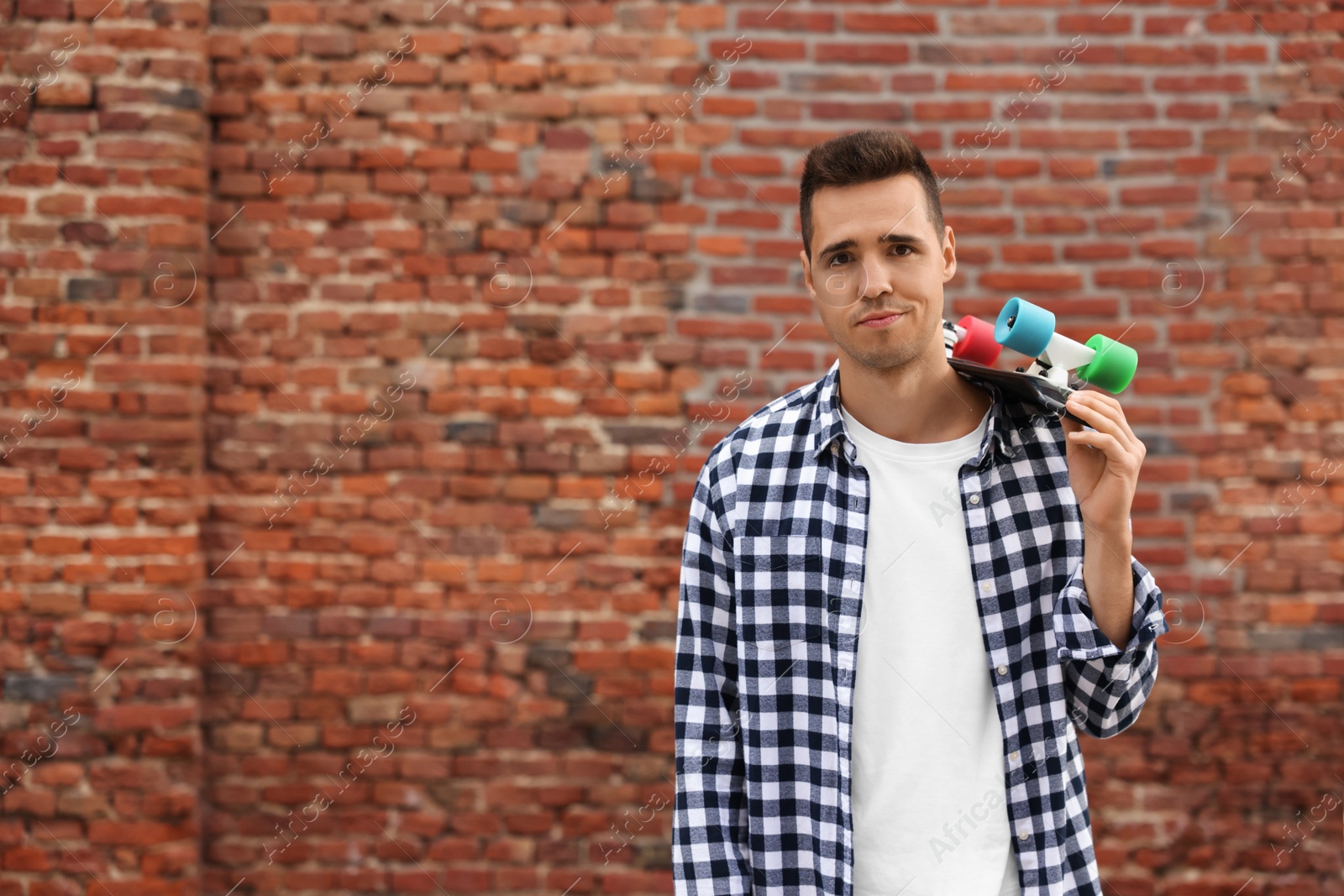 Photo of Portrait of young man with skateboard near brick wall outdoors, space for text. Hip hop dancer