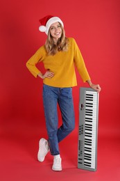 Young woman in Santa hat with synthesizer on red background. Christmas music