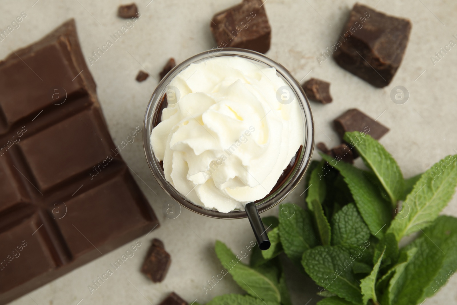 Photo of Glass of delicious hot chocolate with whipped cream, chunks and fresh mint on light table, flat lay