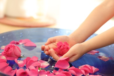 Photo of Child holding rose flower in bowl with water and petals on blurred background, closeup