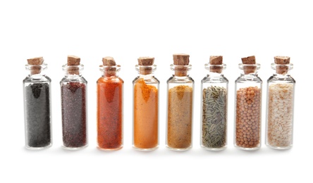 Photo of Row of small glass bottles with different spices on white background