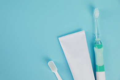 Photo of Electric toothbrushes and toothpaste on light blue background, flat lay. Space for text