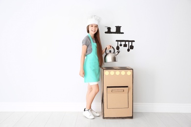 Photo of Little child in chef hat playing with carton stove indoors