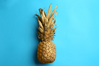 Golden pineapple on light blue background, top view. Creative concept