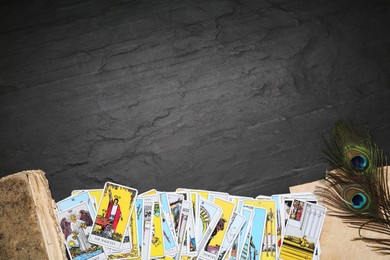 Photo of Tarot cards, old book and peacock feathers on black table, flat lay. Space for text