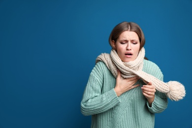 Image of Young woman coughing on blue background, space for text. Cold symptoms