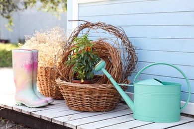 Rubber boots, watering can, baskets and plant near house outdoors. Gardening tools