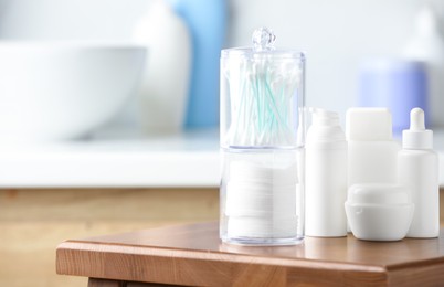 Cotton pads and swabs near cosmetic products on wooden stool in bathroom. Space for text