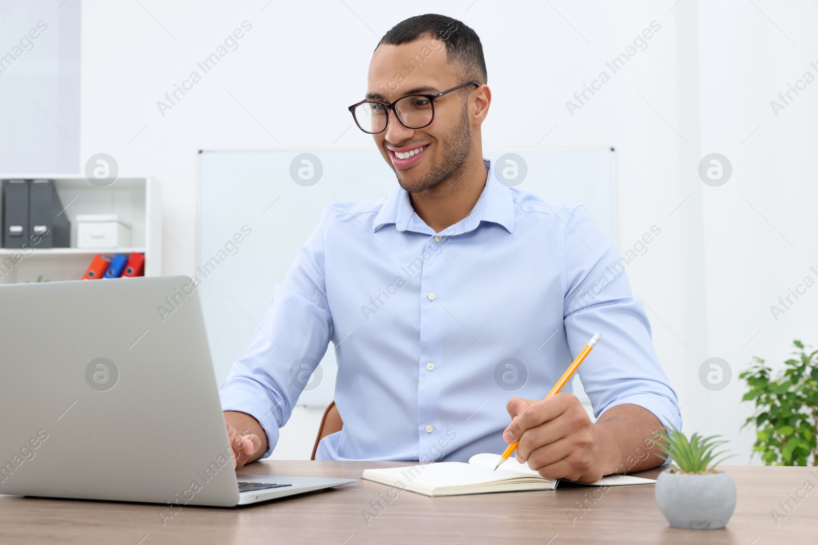 Photo of Happy young intern working with laptop at table in modern office