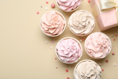 Photo of Delicious birthday cupcakes, gift box and sprinkles on beige background, flat lay. Space for text