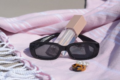Photo of Stylish sunglasses, jewelry and lip gloss on grey surface, closeup