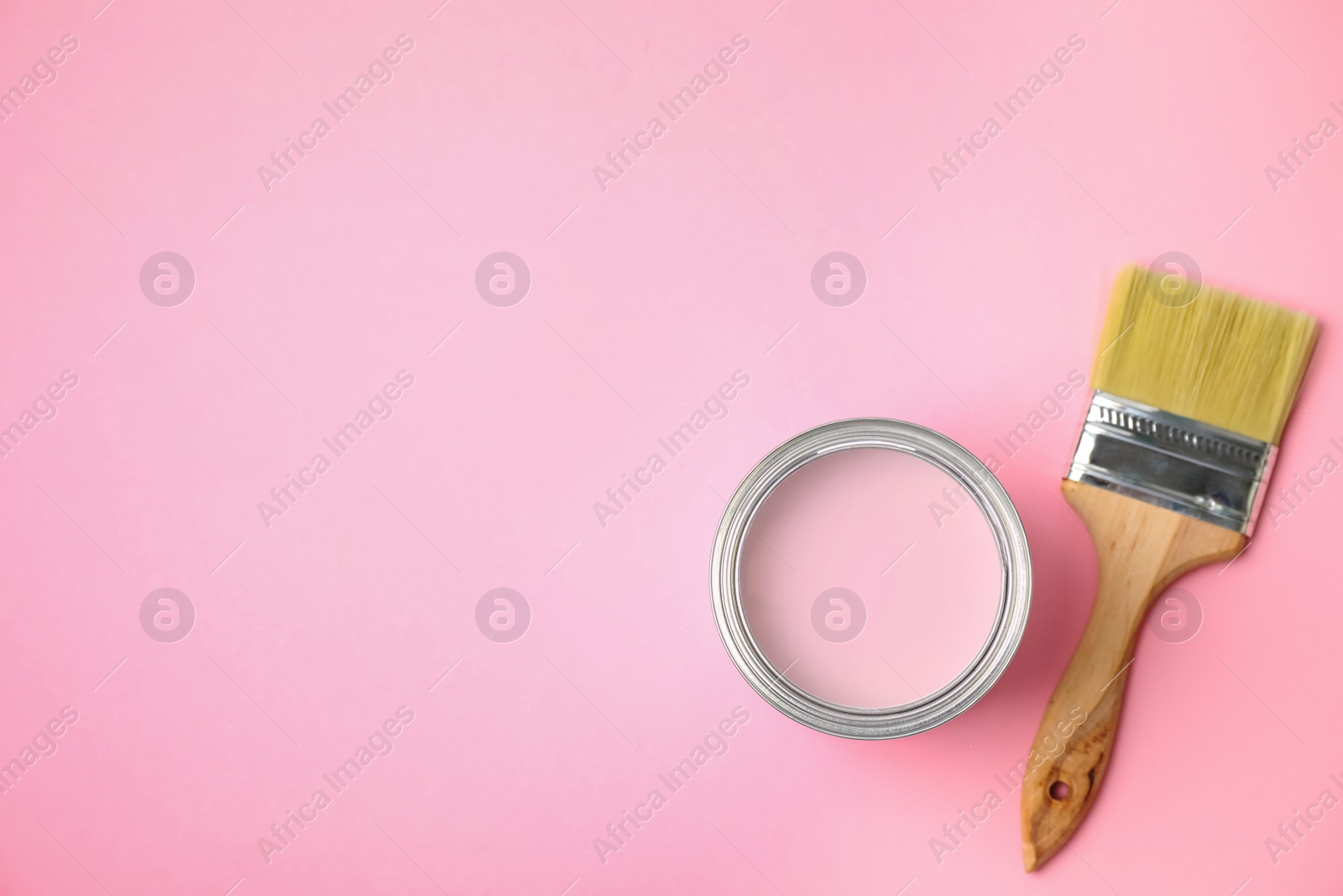 Photo of Open can with paint and brush on pink background, flat lay. Space for text