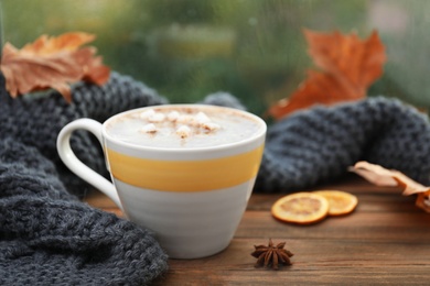 Cup of hot drink and scarf on window sill indoors. Cozy autumn atmosphere