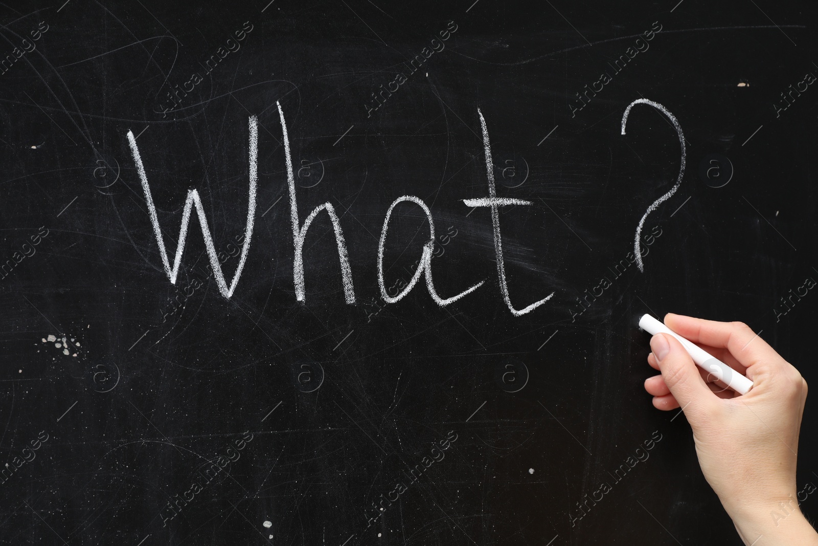 Photo of Woman writing word What? with chalk on blackboard, closeup