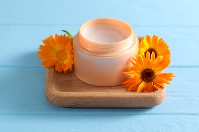 Jar of cream and beautiful calendula flowers on light blue wooden table, closeup