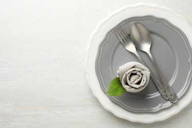 Photo of Stylish setting with cutlery, napkin, leaf and plates on light textured table, top view. Space for text