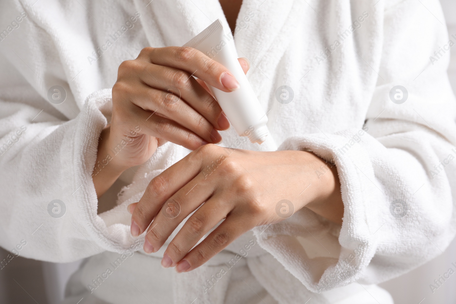 Photo of Woman in bathrobe applying moisturizing hand cream, closeup. Winter skin care cosmetic